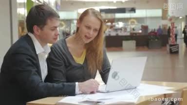 两个商务人士坐在贸易中心的桌子上，讨论他们的新企业热闹的笔记本电脑站在